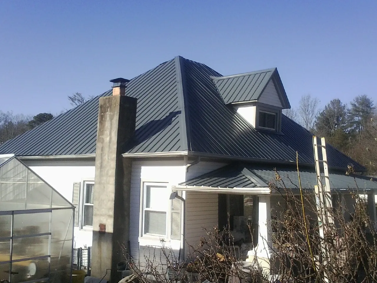 Dark blue standing seam metal roof on a white farmhouse with dormer in Du Pont