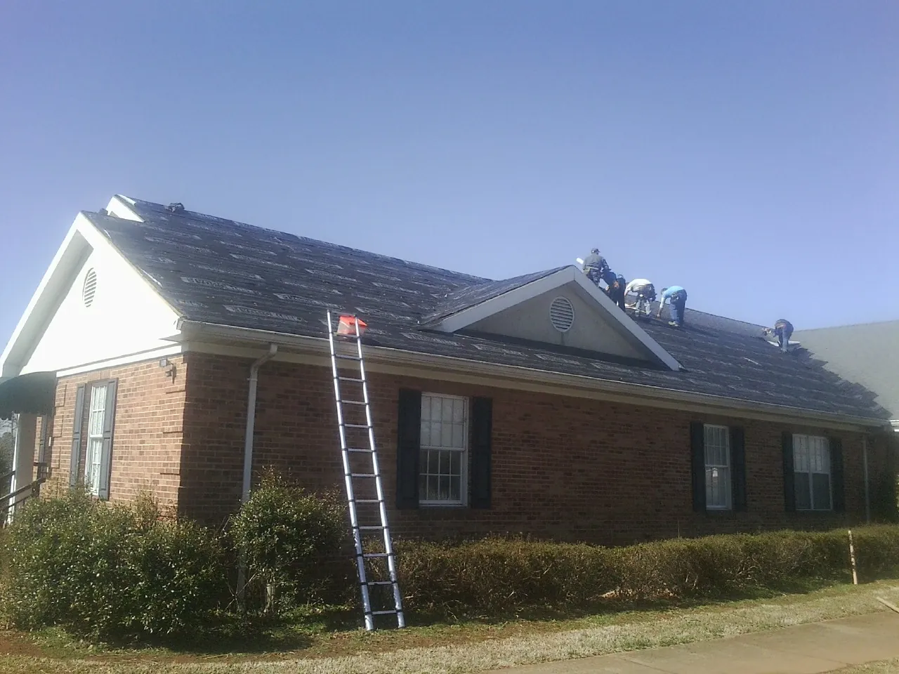 Crew tearing shingles off a brick ranch roof with a ladder set — Emergency Roof Repair work by our crew in Du Pont