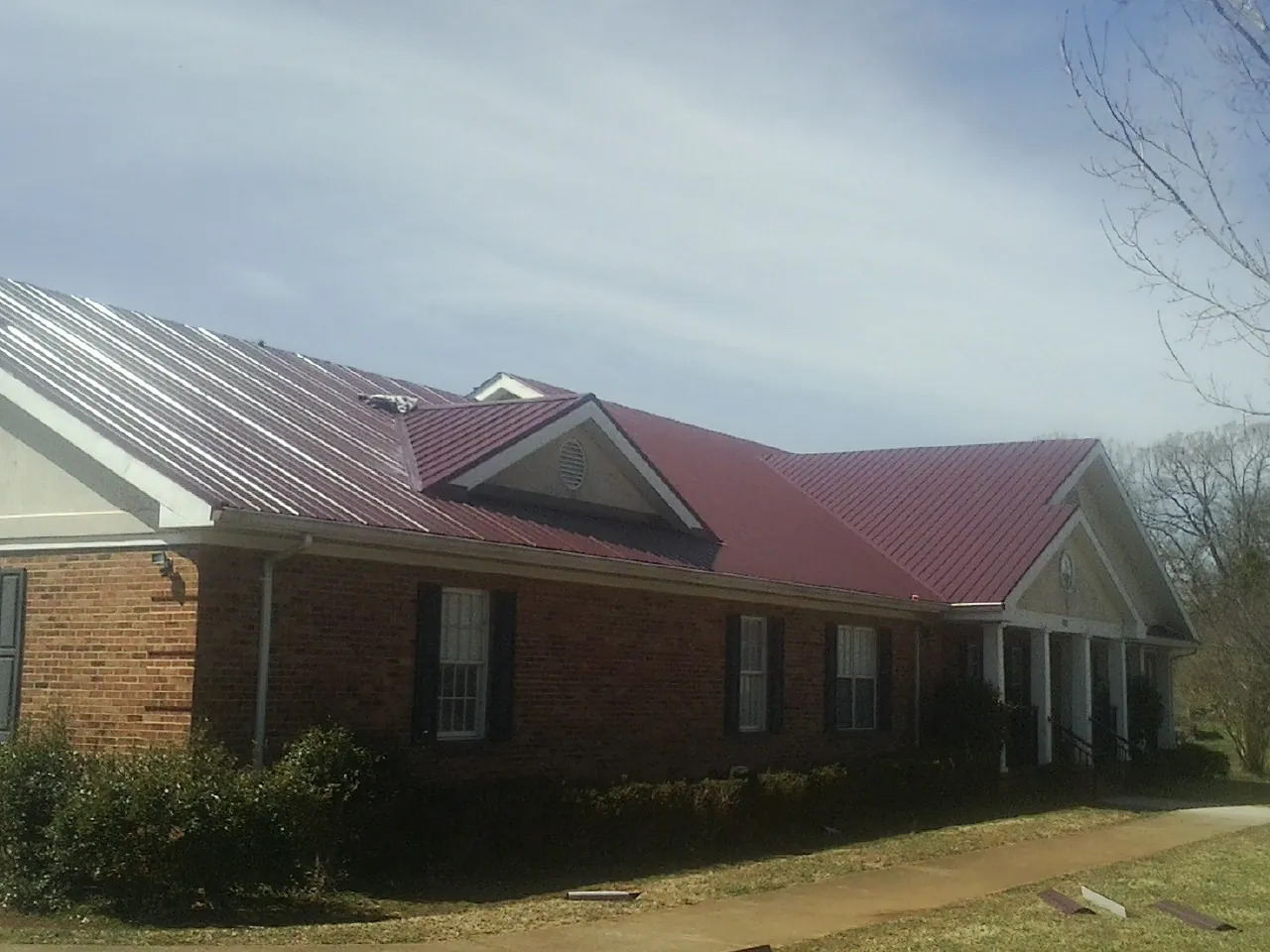 Red metal roof with gabled entries on a long brick building, from a Hail Damage Roof Repair job in Du Pont