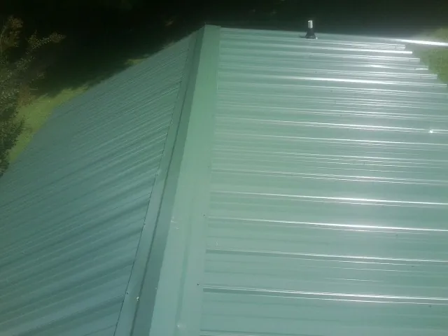 New green metal panels meeting at the ridge of a roof — Flat Roof Repair work by our crew in Du Pont