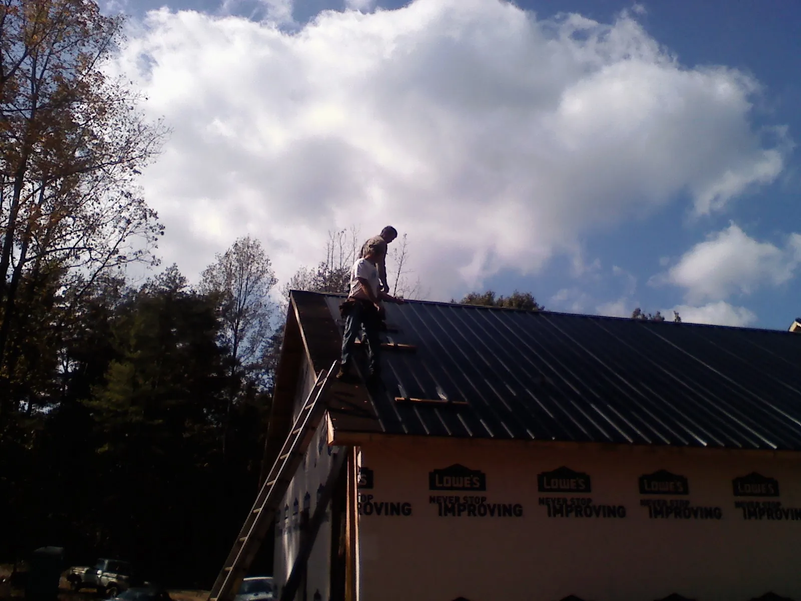 Roofer fastening dark metal panels high against a cloudy sky, from a Roof Inspection job in Du Pont