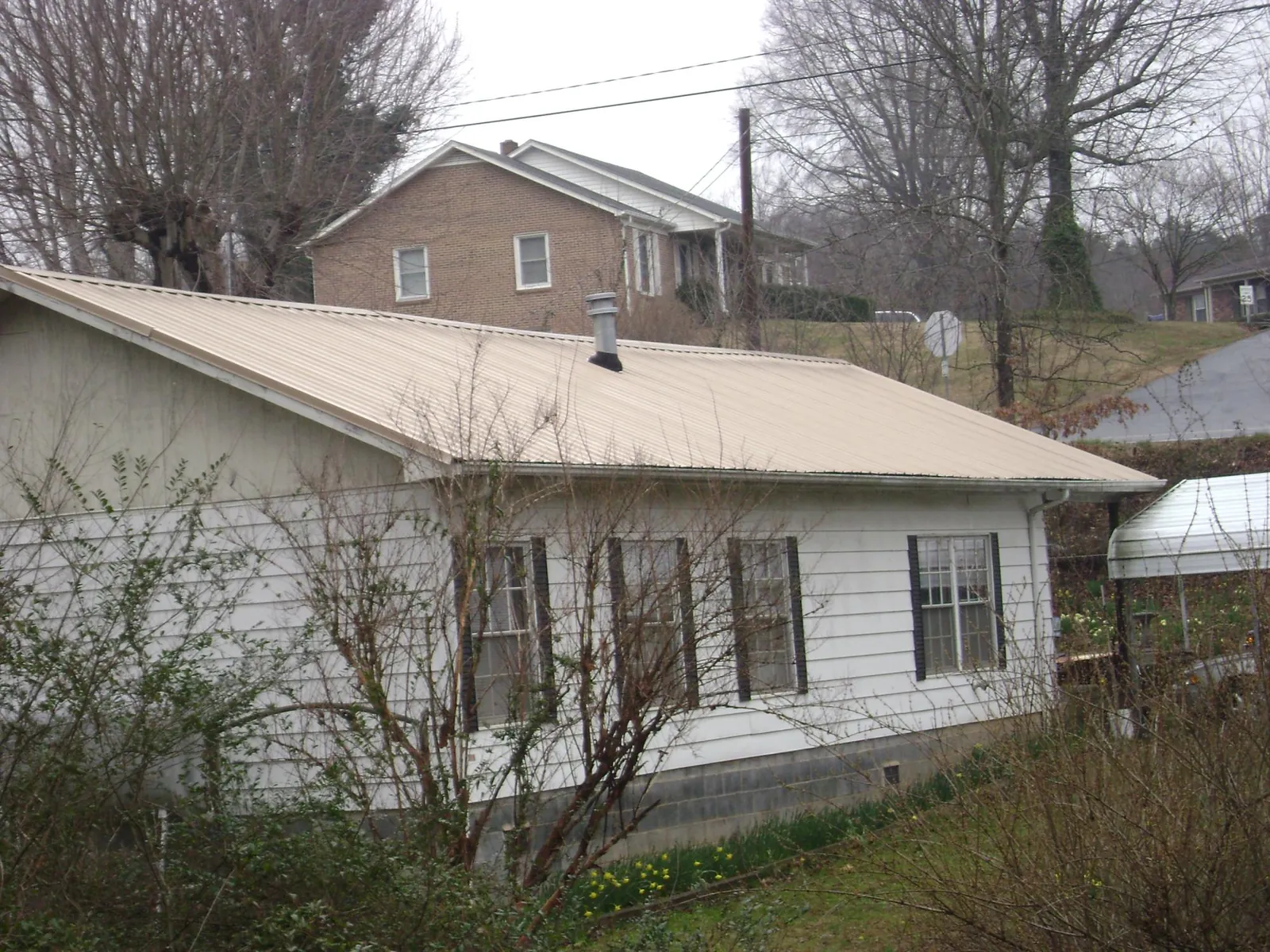 Tan metal roof on a white sided house set into a hillside — Commercial Roofing by Roofing Brothers in Du Pont
